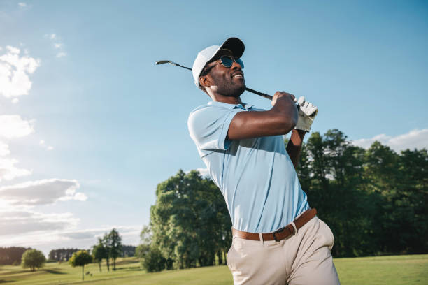 sonriente hombre afroamericano en gorra y gafas de sol jugando al golf - golf club golf golf course equipment fotografías e imágenes de stock