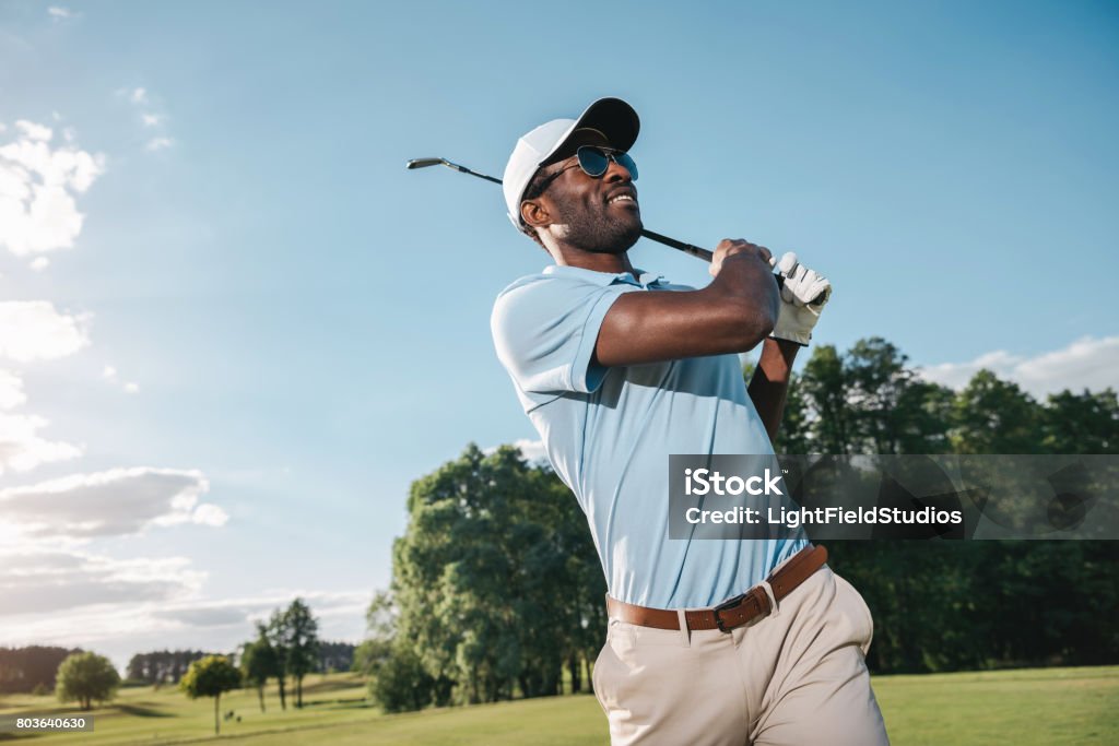 Smiling african american man in cap and sunglasses playing golf Golf Stock Photo