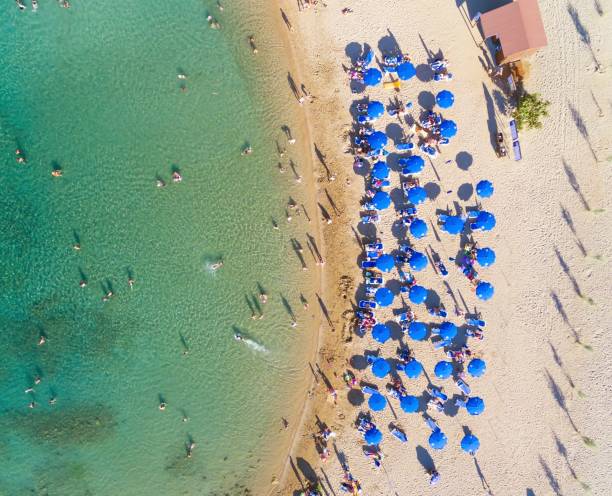 Aerial bird's eye view of sandy beach in Protaras, Famagusta, Cyprus island at the Agia Triada bay. Sun umbrellas, sea beds and silhouette of people sunbathing and swimming during the summer holiday heat