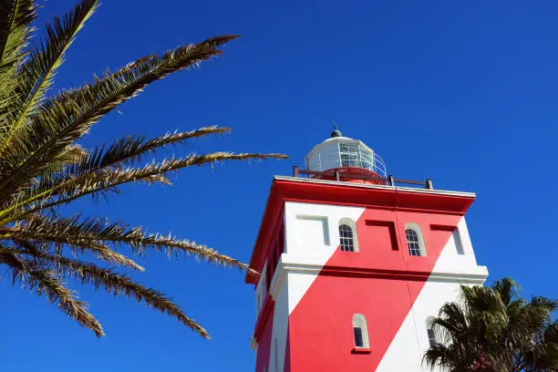 Greenpoint (also known as Mouille Point) lighthouse, with its distinctive red and white diagonal stripes, seen from gound level on a sunny day.