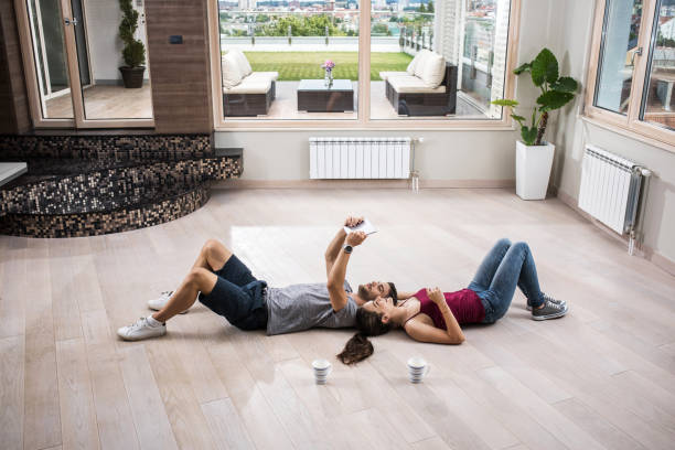 istock Young couple lying on parquet floor and using touchpad in their new penthouse. 803670202
