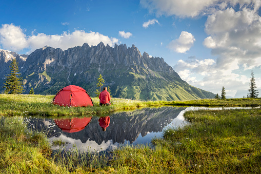 Camper in front of his tent with reflection in a pond at Hochkönig, Mandelwand