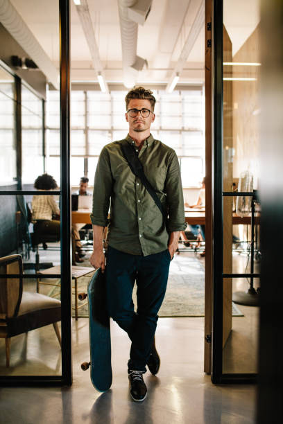 istock Young man with skateboard in office doorway 803690382