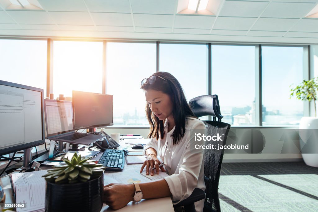 Woman entrepreneur at work in office. Businesswoman studying business papers on her desk. Woman working in office sitting at her desk. Desk Stock Photo