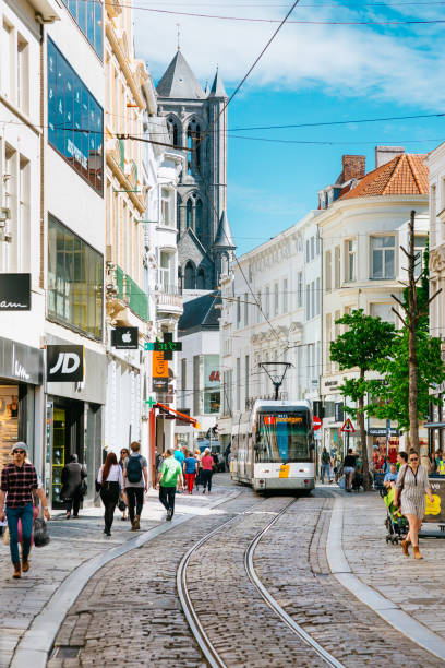 Lovely spring day in Ghent - people walking on a street full of different shops. The Graslei and St Nicholas Church on the background.