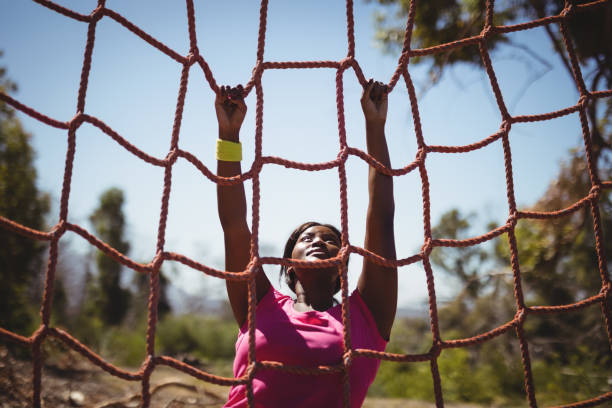 Determined woman climbing a net during obstacle course Determined woman climbing a net during obstacle course in boot camp obstacle course stock pictures, royalty-free photos & images