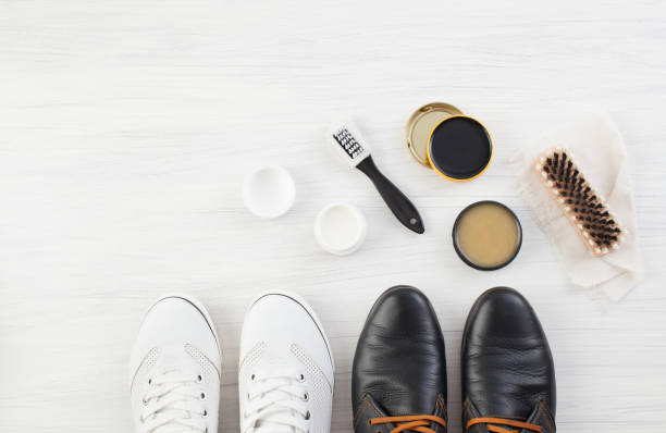 Two pairs of shoes, Shoe Polish and brush on white Care for leather shoes over white wooden background. The background image place for text. leather care stock pictures, royalty-free photos & images