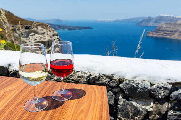 Two glasses of wine & Aegean sea & volcano Horizontal color image of two glasses of wine - white wine & rose wine. Aegean sea and volcano in the background. table ledge stock pictures, royalty-free photos & images