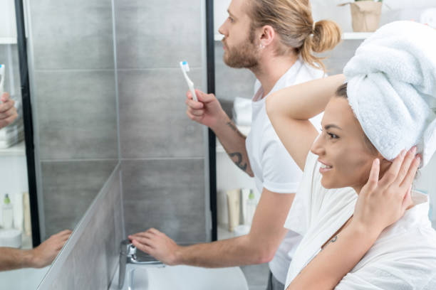 istock Smiling young woman with towel on head looking at mirror while husband brushing teeth behind 803790360