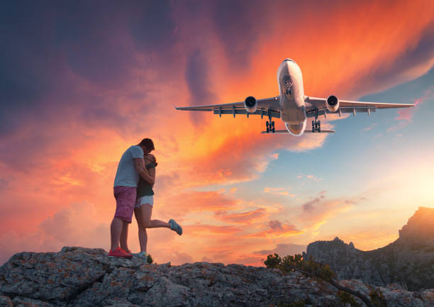 avion et étreindre et embrasser l’homme et la femme sur le sommet de la montagne au coucher du soleil. paysage avec atterrissage avion de passager, jeune couple et le ciel coloré. avion commercial vole dans le ciel orange - leaving business landscape men photos et images de collection