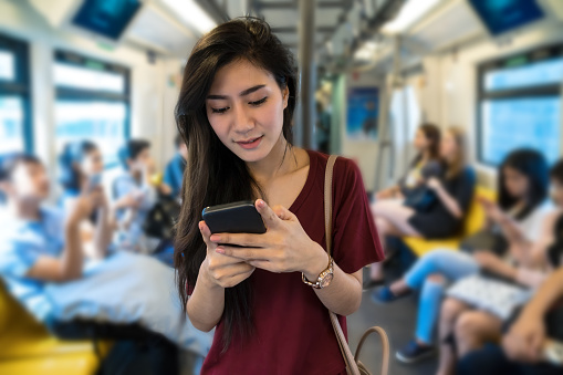 Asian woman passenger with casual suit using the social network via smart mobile phone in the BTS Skytrain rails or MRT subway for travel in the big city, lifestyle and transportation concept