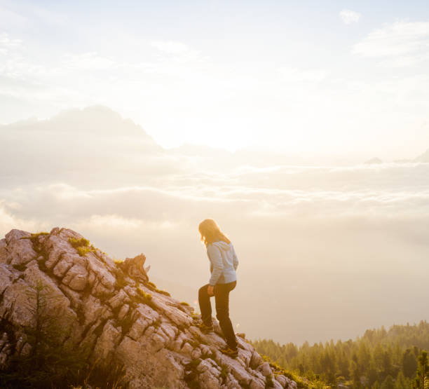 istock Woman on top of mountain peak with soft clouds floating below 803822172