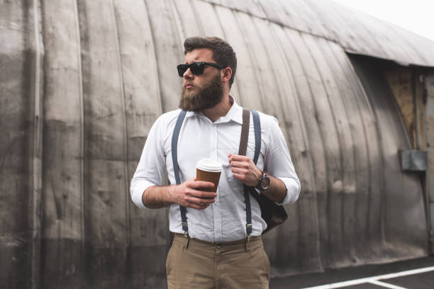 istock fashionable bearded man with sunglasses and leather backpack holding disposable coffee cup 803837092