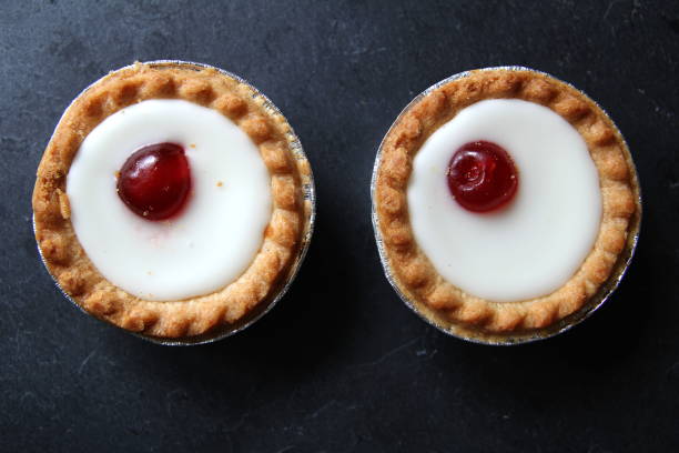 istock Cherry bakewell tarts in foil case on dark background looking like eyes 803849832
