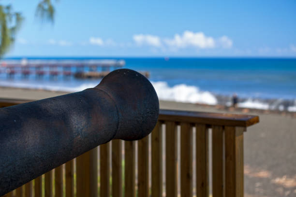 Old cannon with in the background, the Débarcadère de Saint-Paul (Landing of Saint-Paul) with the waves of the summer solstice.