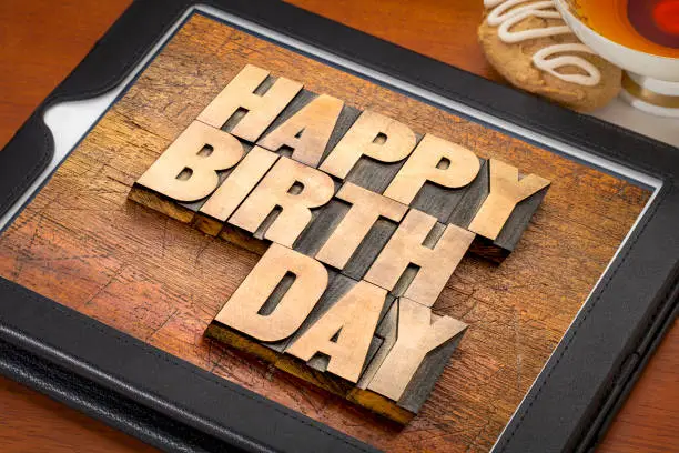 Happy birthday greeting card - word abstract in letterpress wood type on digital tablet with a cup of tea and cookie