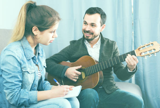 istock guitar tutor explaining basics to his female client at home 803894822