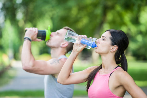 mann und frau trinkwasser in einem park im sommer - exercising sensuality water bottle relaxation exercise stock-fotos und bilder