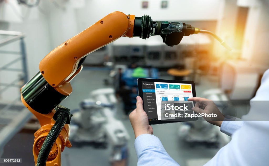 Engineer hand using tablet, heavy automation robot arm machine in smart factory industrial with tablet real time monitoring system application. Industry 4th iot concept. Computer-Aided Manufacturing Stock Photo