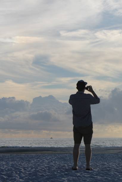 istock Man on beach photographing sunset 803987764