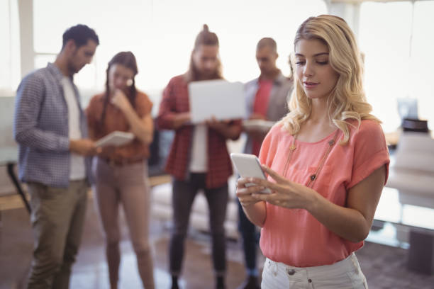 istock Young woman using mobile phone with team working in background 804025006