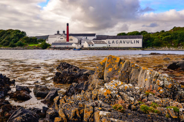 海の海岸線の前景、アイラ、イギリスでのラガヴーリン蒸留所工場 - bruichladdich whisky ストックフォトと画像