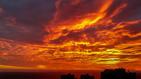 Dramatic bloody red orange colored sky sunset above silhouette of cityscape buildings Haifa city and Mediterranean Sea