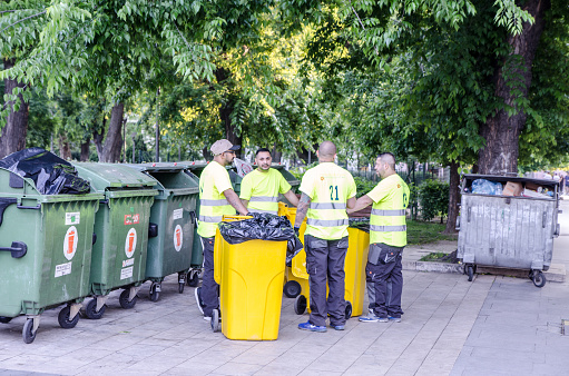 City blue collar workers having a pause around wheeled garbage cans during summer day in Budapest