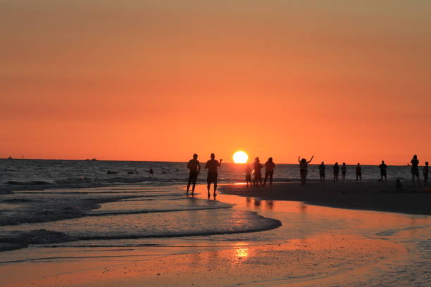 People waiting for sunset, Treasure Island, Florida. Groups of people on the each and in the water. Low sun, beautiful orange sky.