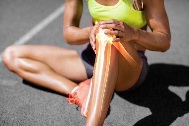 Low section of sportswoman suffering from knee pain Low section of sportswoman suffering from knee pain while sitting on track during sunny day low quality of life stock pictures, royalty-free photos & images