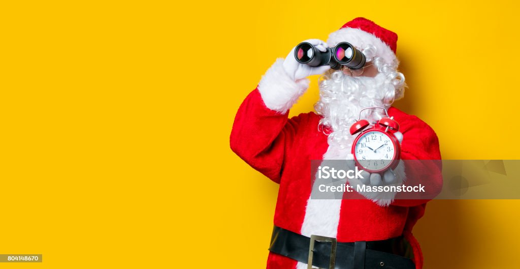 Santa Claus holding binoculars and alarm clock Funny Santa Claus holding binoculars and alarm clock on yellow background Santa Claus Stock Photo Santa Claus holding binoculars and alarm clock Funny Santa Claus holding binoculars and alarm clock on yellow background Santa Claus Stock Photo
