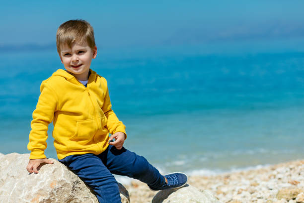 bambino sorridente seduto su una roccia con paesaggio marino sullo sfondo - student outdoors clothing southern africa foto e immagini stock