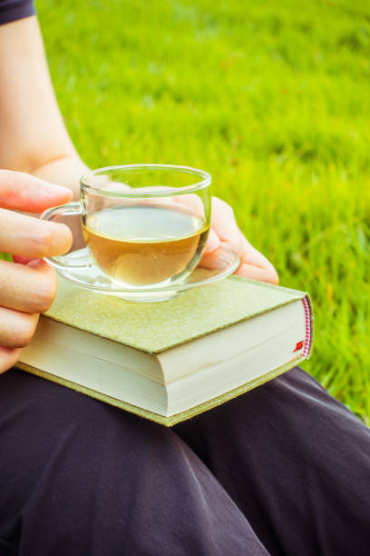 istock woman sitting on grass holding tea and book 804219050