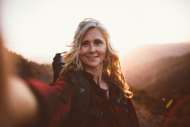 Happy senior woman hiker taking a selfie on mountain edge Active senior woman hiker standing on top of mountain taking a selfie at sunset eco tourism photos stock pictures, royalty-free photos & images