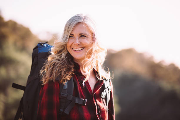 Cheerful active senior woman with grey hair carrying backpack and hiking in nature