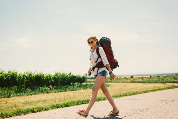Woman on the road trip. Walking alone with backpack on her back on the road.