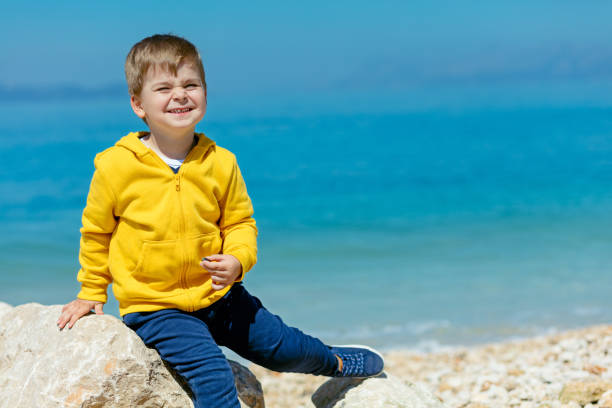 bambino sorridente seduto su una roccia con paesaggio marino sullo sfondo - student outdoors clothing southern africa foto e immagini stock