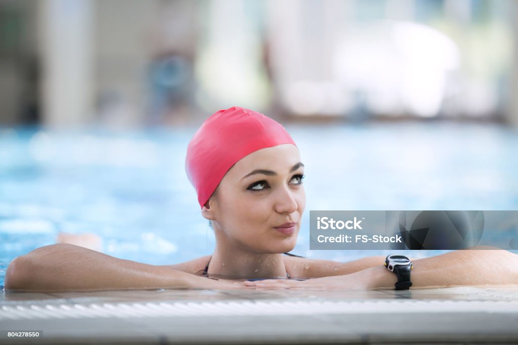 Cap belle femme souriant à la caméra en regardant bordure de piscine - Photo de Bonnet de bain libre de droits