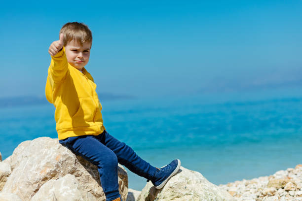 bambino sorridente seduto su una roccia con paesaggio marino sullo sfondo - student outdoors clothing southern africa foto e immagini stock