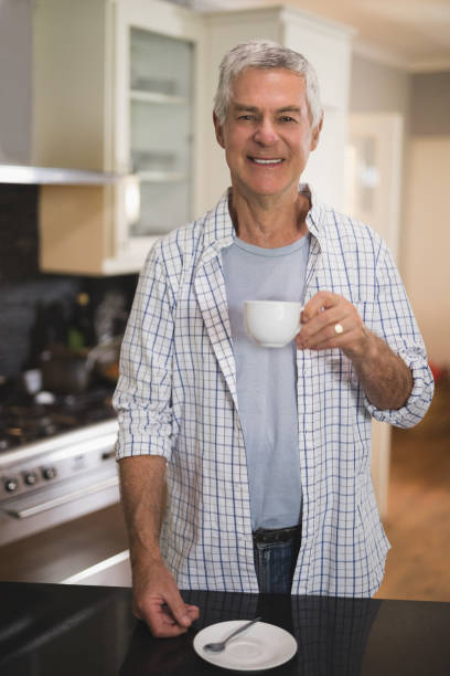 istock Smiling senior man holding cup while standing in kitchen at home 804295546