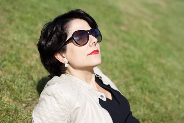 latin woman with sunglasses turning her face toward the sun while relaxing on lawn