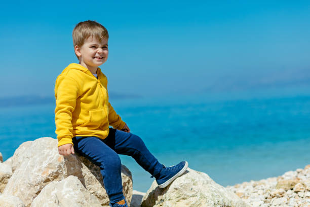 bambino sorridente seduto su una roccia con paesaggio marino sullo sfondo - student outdoors clothing southern africa foto e immagini stock