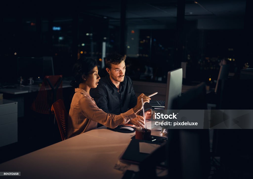 Making the extra hours count in their favour Shot of two businesspeople working late in an office Office Stock Photo