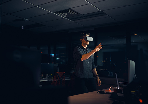 Shot of a businessman wearing a VR headset while working late in an office