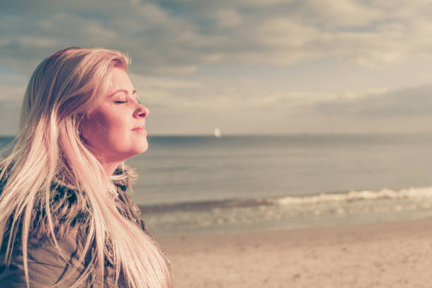 Leisure, spending free time outside, healthy walks concept. Woman wearing warm jacket relaxing on beach near sea, cold sunny day