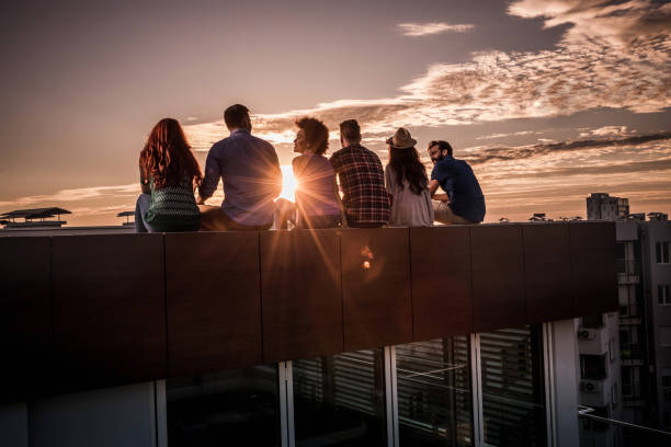 istock Back view of group of friends talking on a rooftop at sunset. 804350800