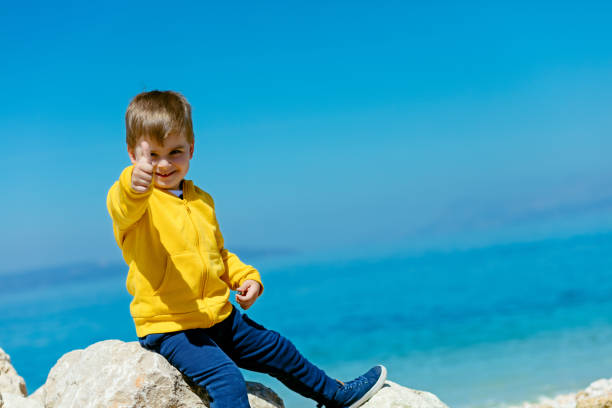 bambino sorridente seduto su una roccia con paesaggio marino sullo sfondo - student outdoors clothing southern africa foto e immagini stock