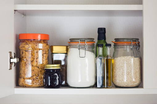 stocked kitchen pantry with food - jars and containers of cereals, jam, coffee, sugar, flour, oil, vinegar, rice