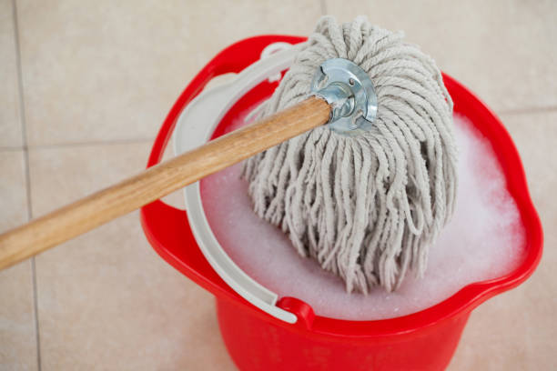 Red bucket with foamy water and mopping the tile floor