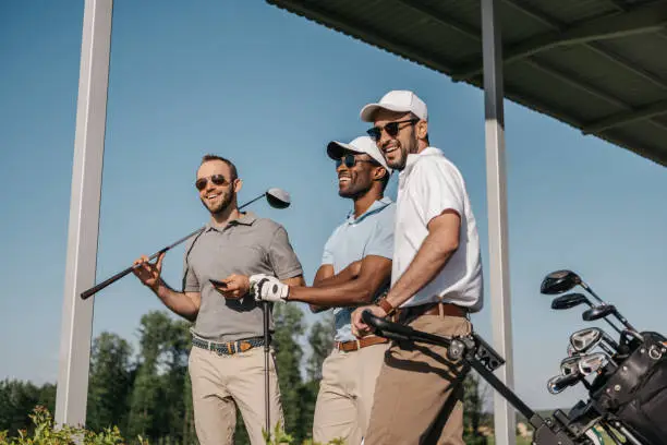 Three smiling men in sunglasses holding golf clubs outdoors
